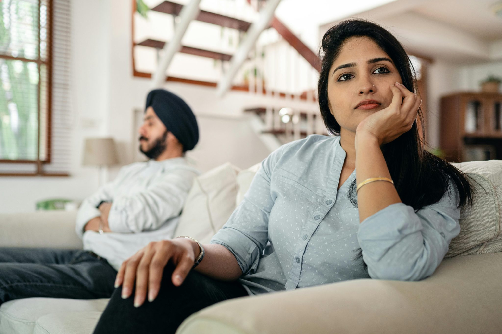 A Sikh couple looking away from each other whilst sat on a sofa